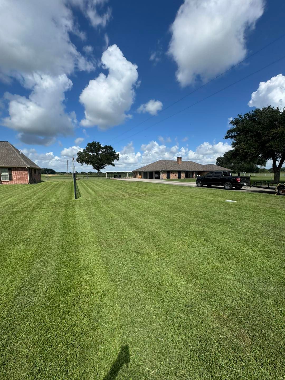Green lawn with striped mowing pattern, several buildings, blue sky with puffy white clouds.