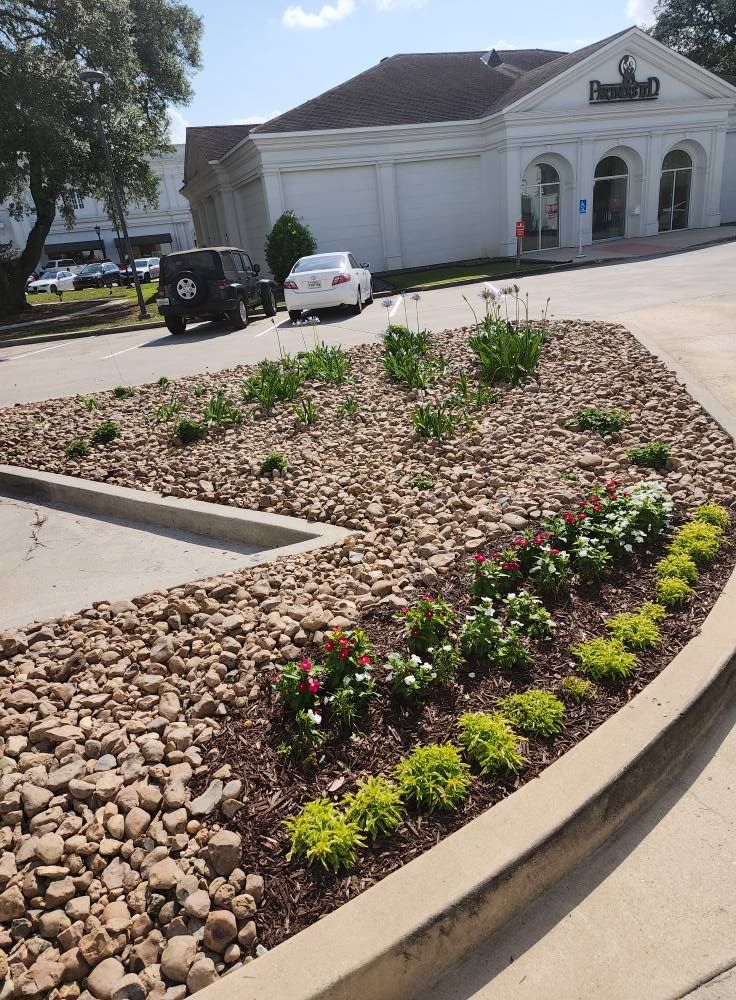 Landscaped bed with tan rocks and colorful flowers in front of a white building with arched windows.