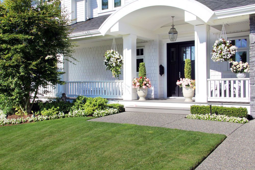 Well-manicured lawn and garden leading to a white porch with hanging flower baskets and a black front door.