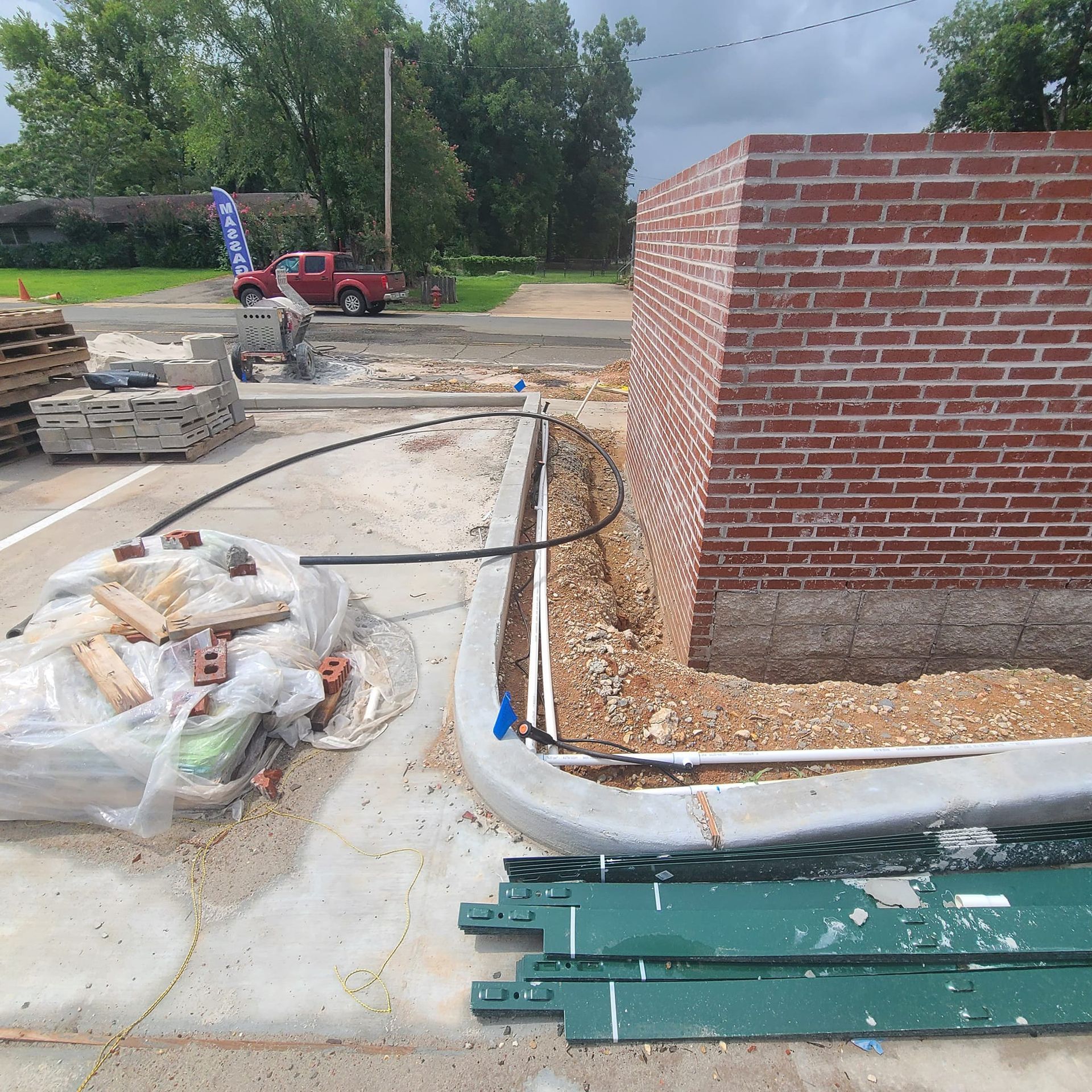 Construction site with a brick wall, curb, materials, and a pickup truck.