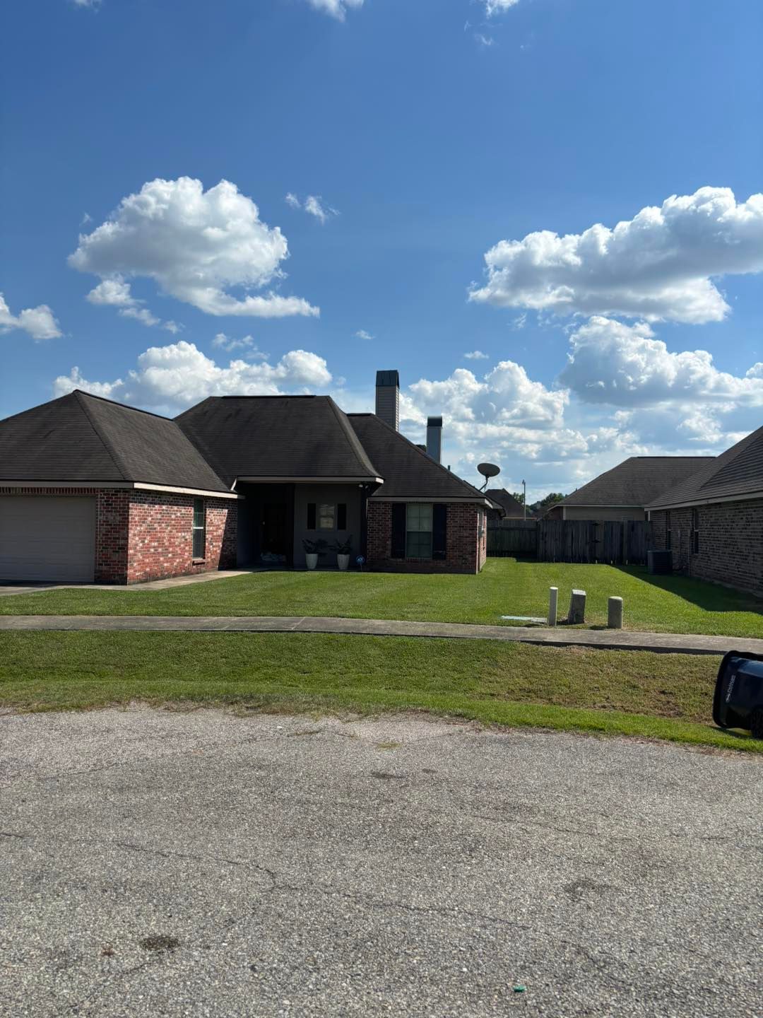 A brick house with a dark roof and green lawn under a partly cloudy blue sky.