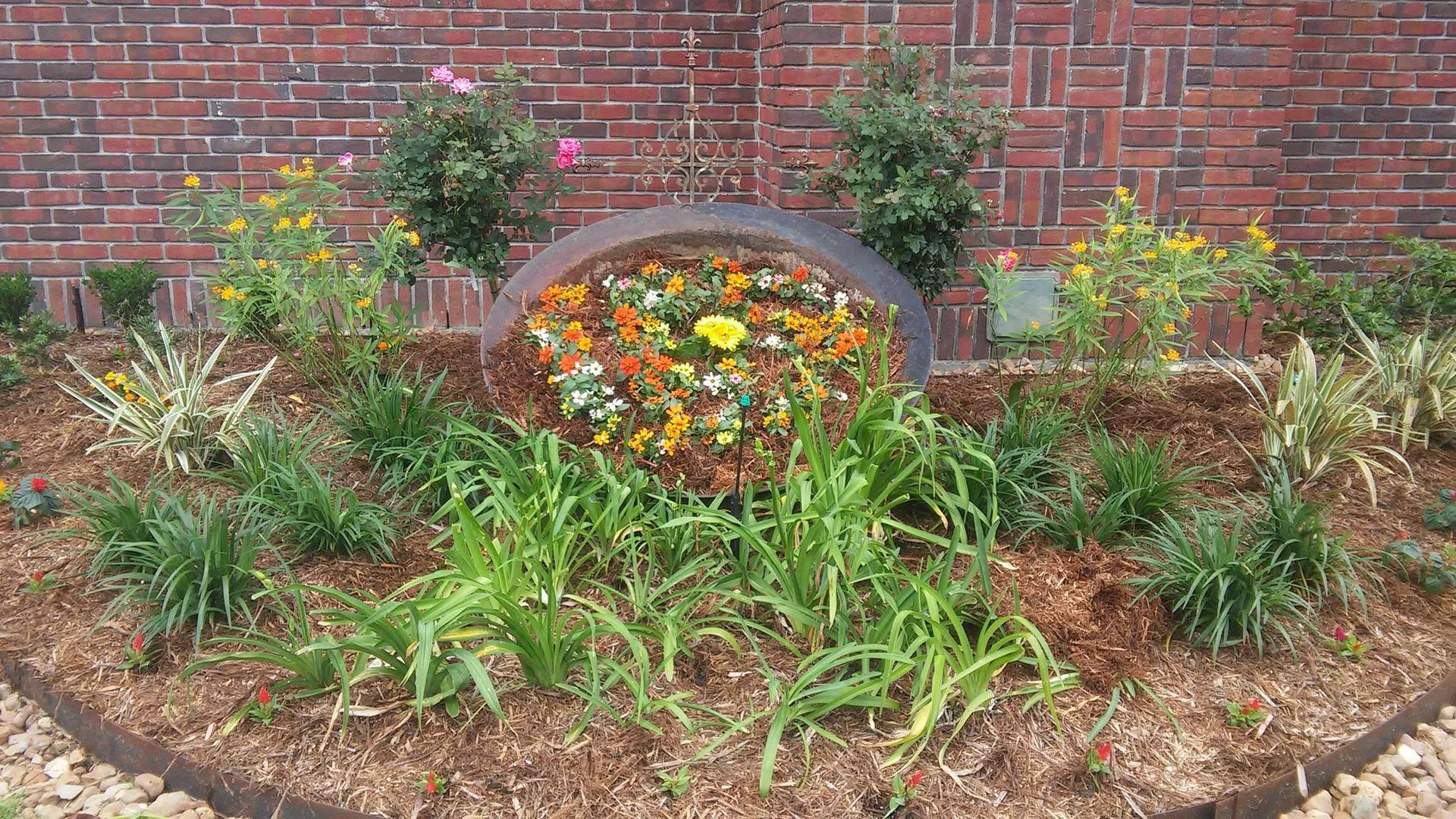 Flower garden in front of a brick wall, featuring colorful flowers and green plants.