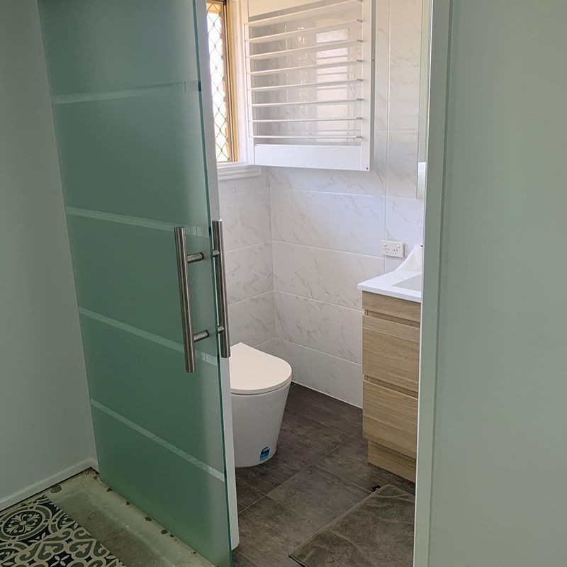 Bathroom With a Toilet and Sliding Glass Door — Moore Park Beach Glass & Security in Moore Park Beach, QLD
