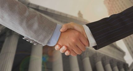 Two men shaking hands in front of a building.
