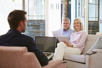 A business attorney is sitting on a chair talking to a woman and a man.