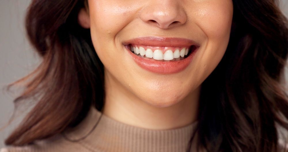 Close-up of a smiling person with dark hair wearing a beige ribbed turtleneck sweater.