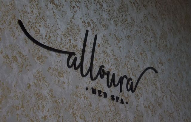 Black “alloura” script logo on a textured beige wall