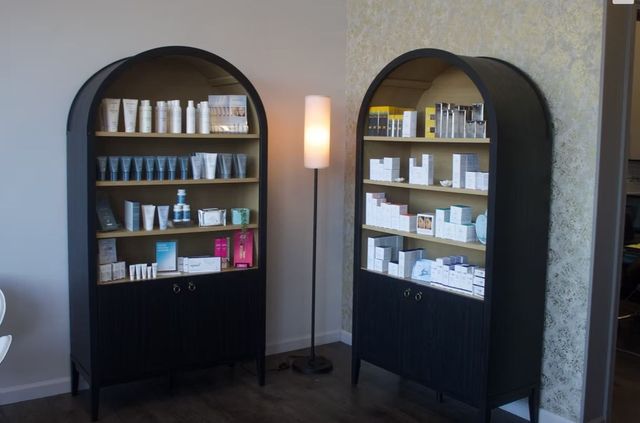 Two black arched shelves with skincare products beside a tall floor lamp in a room