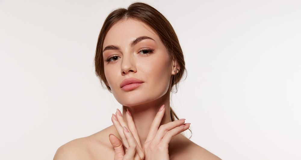 Portrait of a woman with hands near her neck against a light background