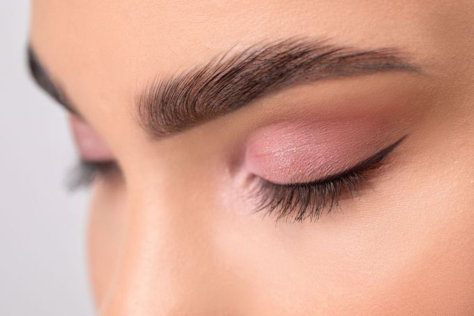 Close-up of a closed eye with pink eyeshadow, winged eyeliner, and well-defined eyebrow