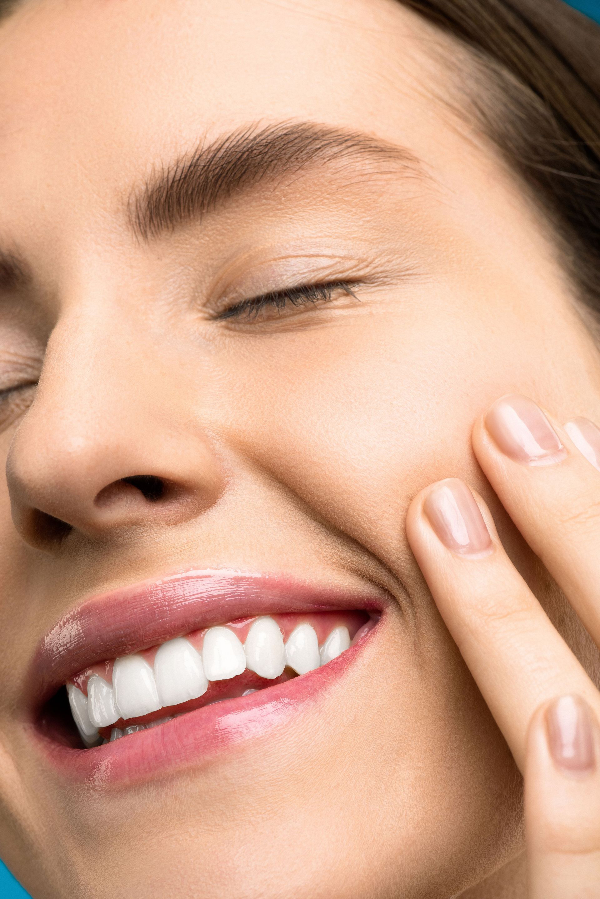 Close-up of a smiling woman touching her cheek with bare skin and pink lipstick