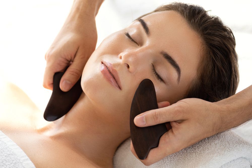 Woman receiving a facial massage with warm black stones on her neck and face
