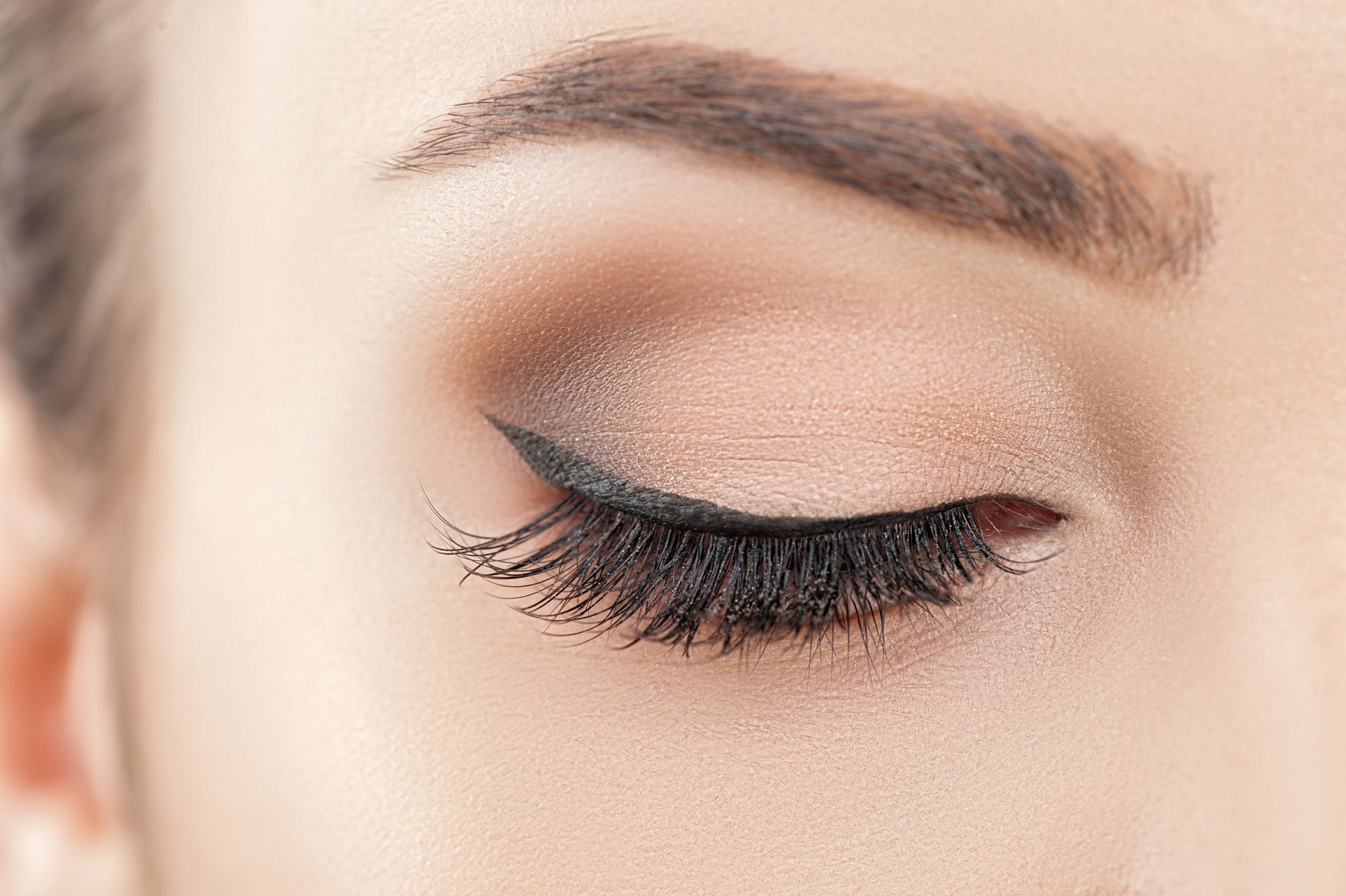 Close-up of a closed eye with long black eyelashes and soft beige eyeshadow
