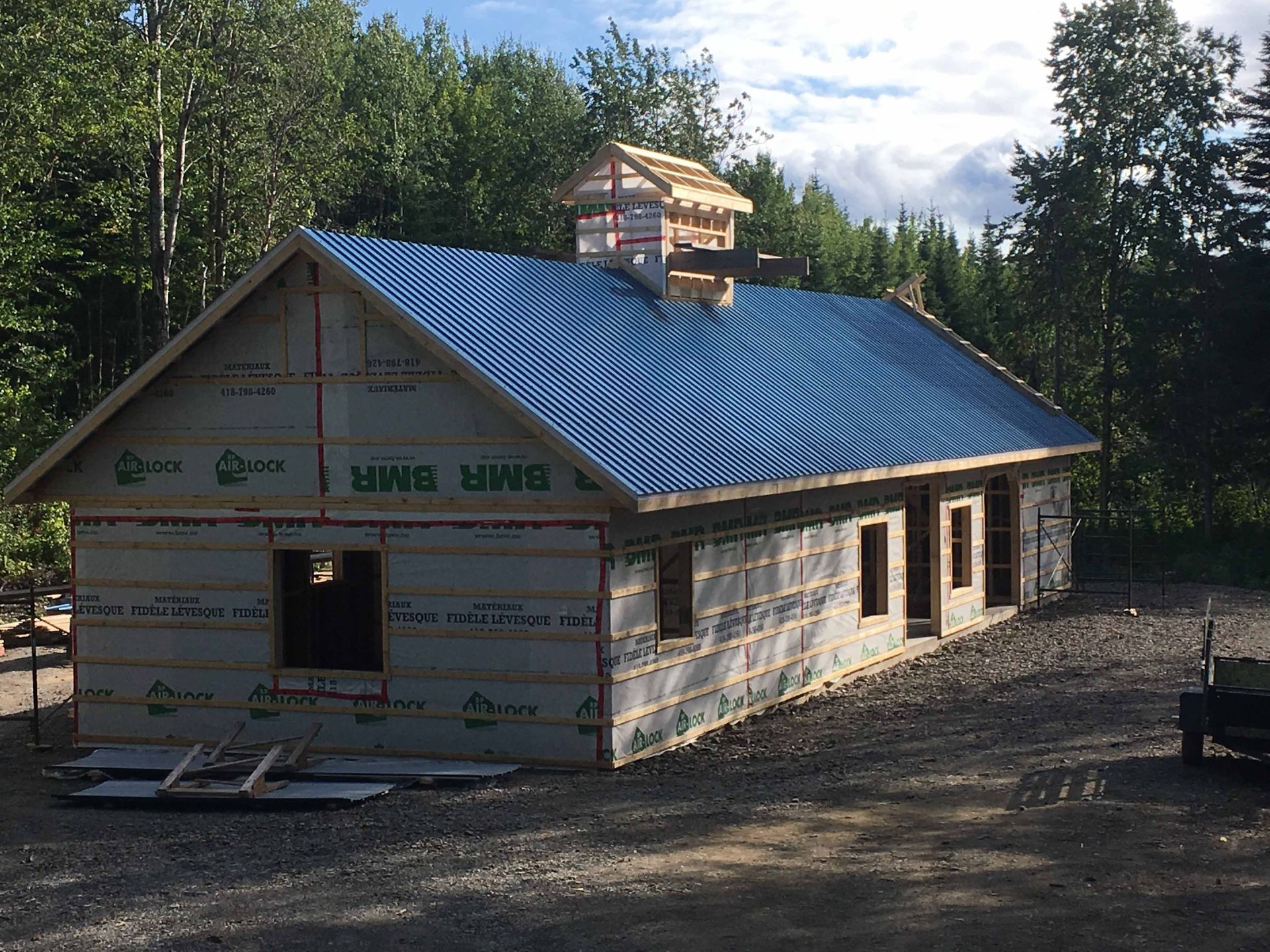 Maison partiellement construite avec toit en métal bleu dans une zone boisée