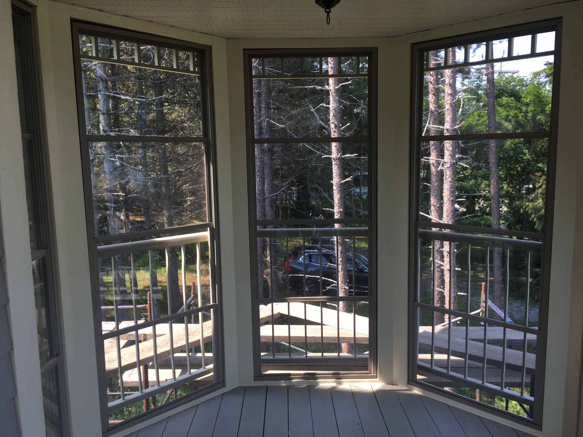Baie vitrée donnant sur un jardin ensoleillé avec des arbres et une terrasse en contrebas