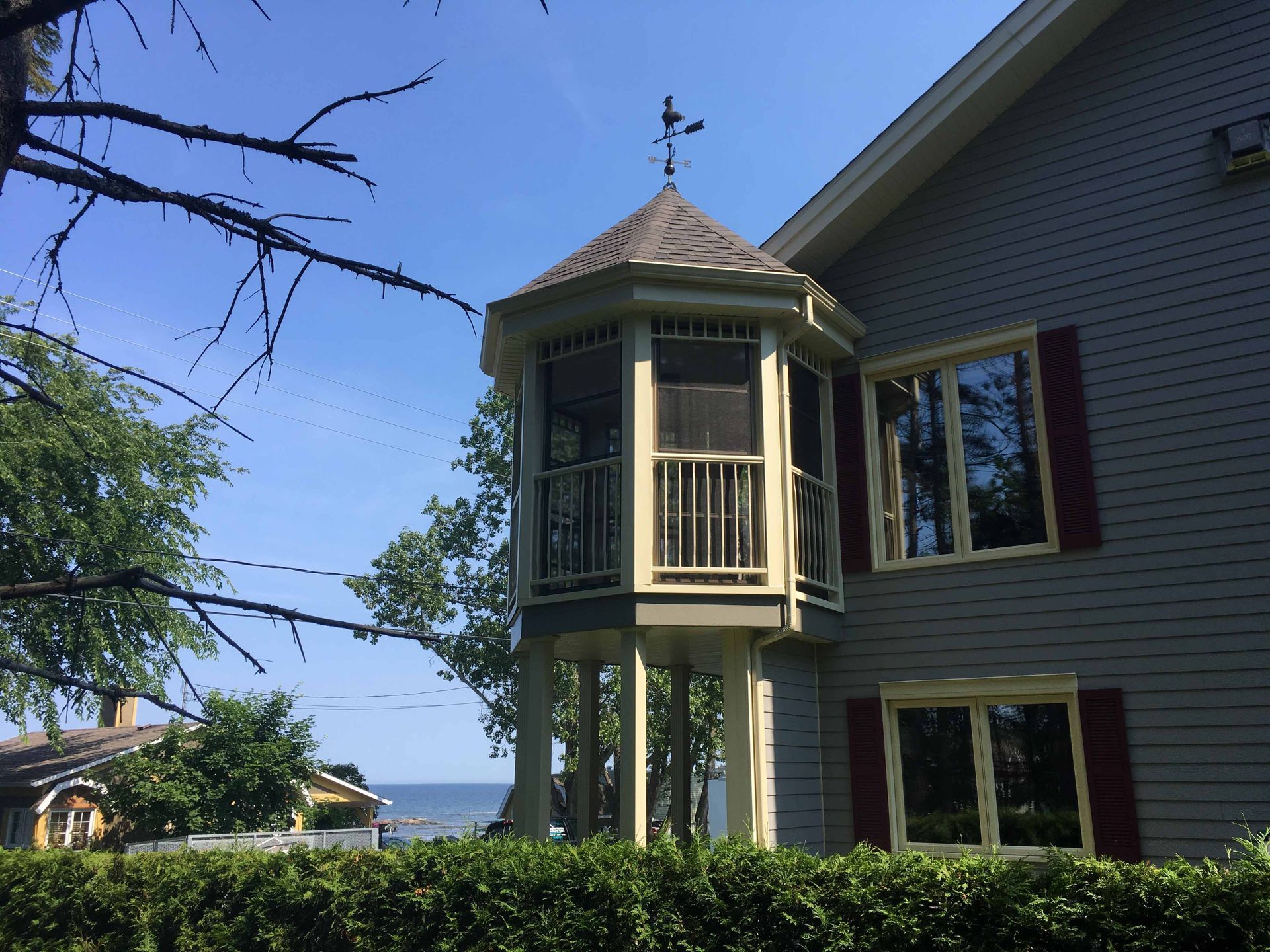 Chambre dans une tour octogonale d'une maison grise surplombant l'eau, encadrée par des arbres et un ciel bleu.