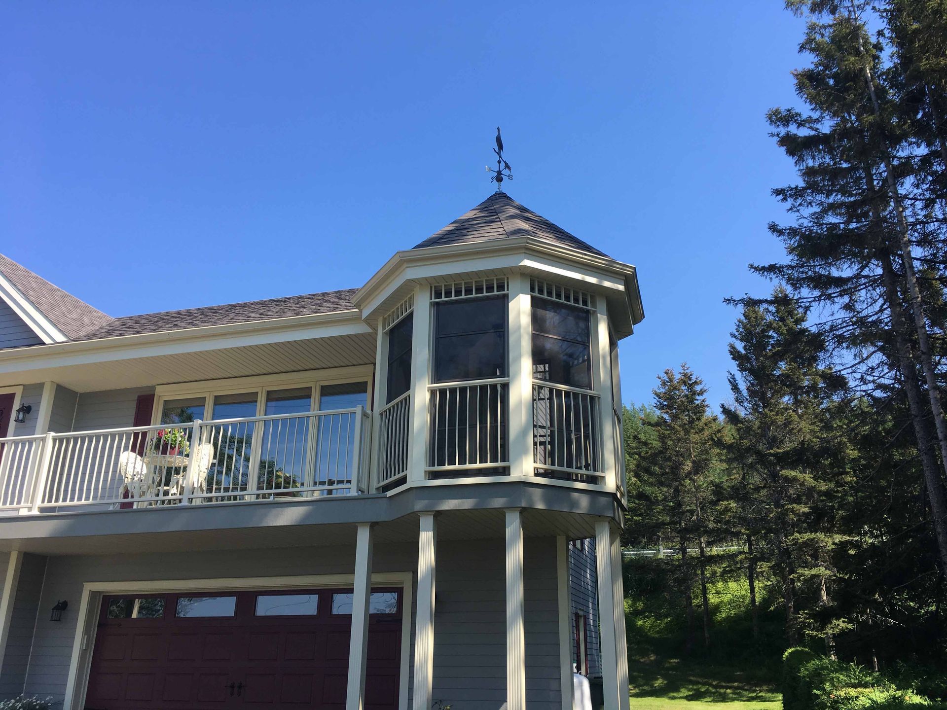 Extérieur de la maison avec porche couvert, baie vitrée et garage sous un ciel bleu clair