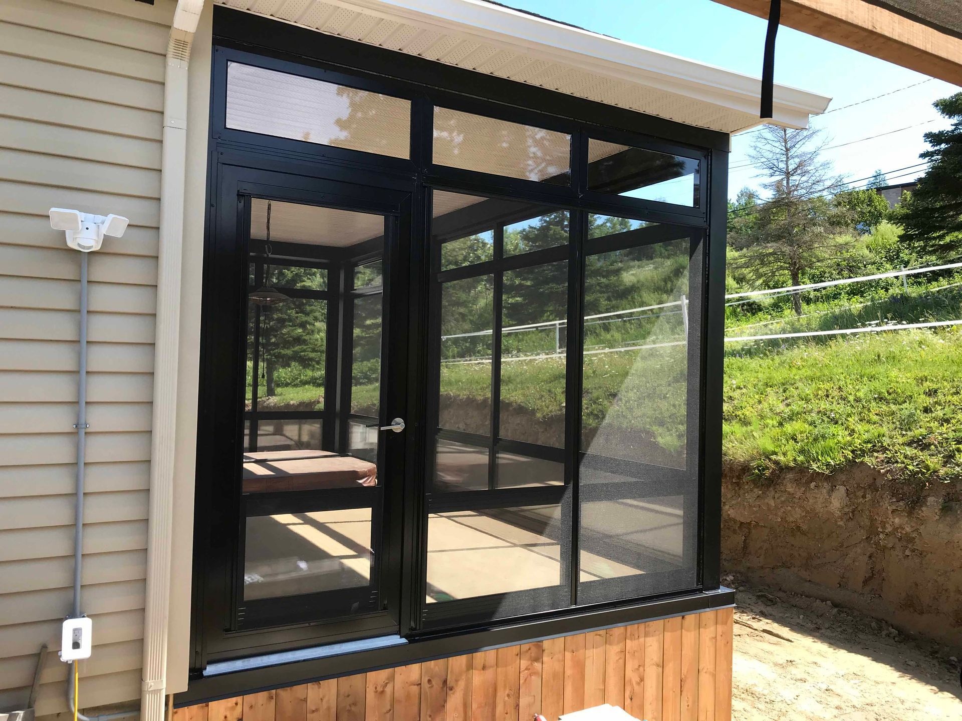Véranda vitrée à cadre noir, avec fenêtres moustiquaires et base en bois.