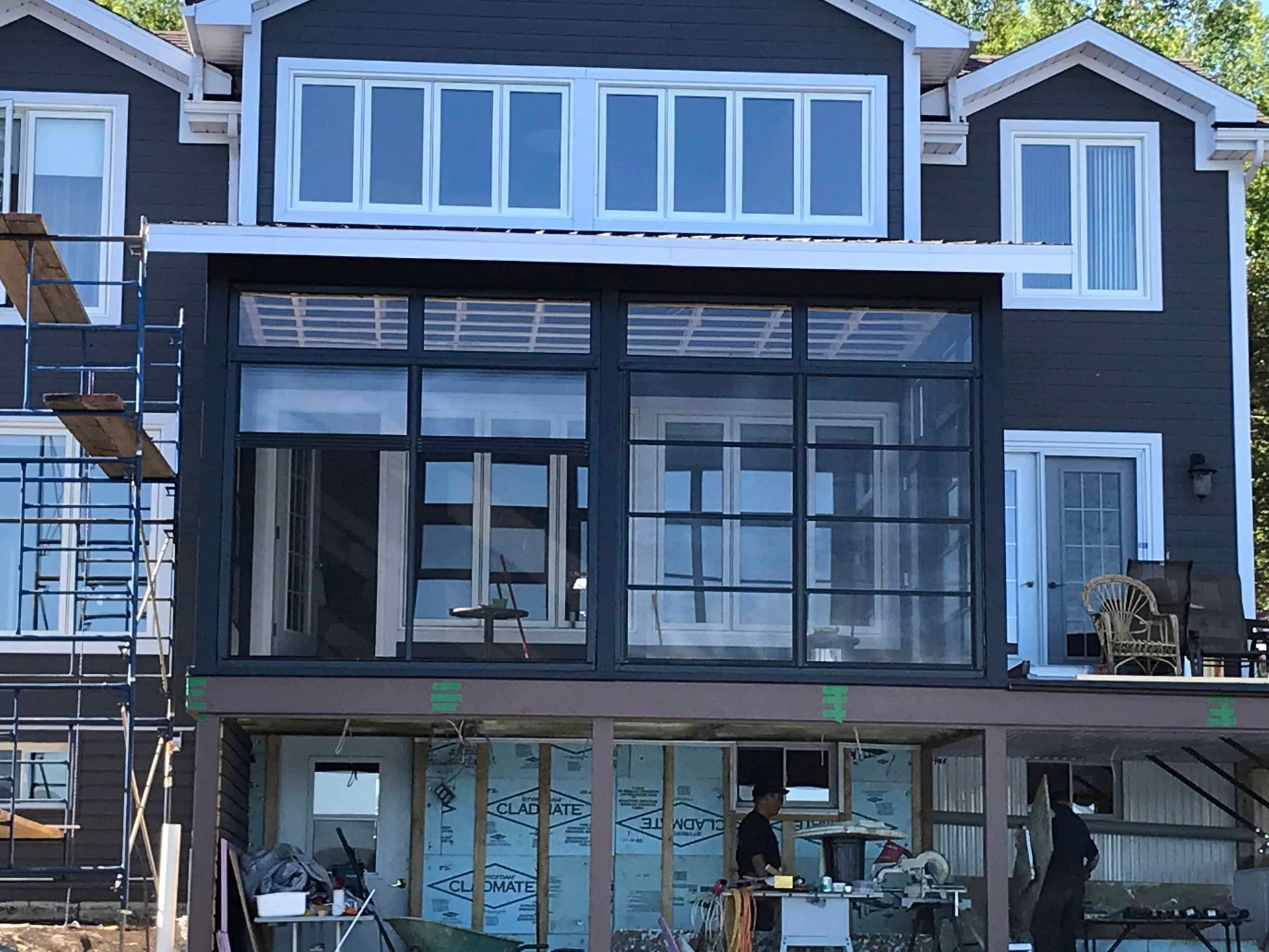 Maison moderne gris foncé avec de grandes fenêtres et un porche en construction, avec des échafaudages sur la gauche.