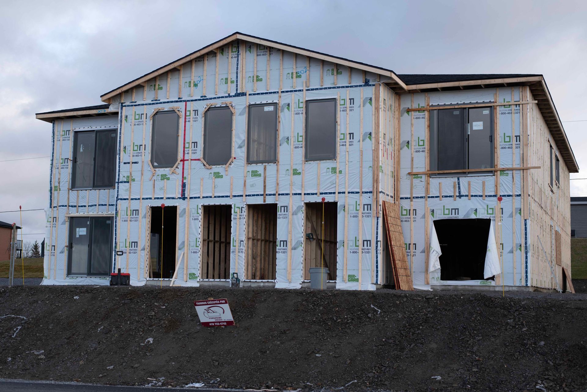 Maison à deux étages partiellement construite, avec bardage apparent et fenêtres et portes non finies.