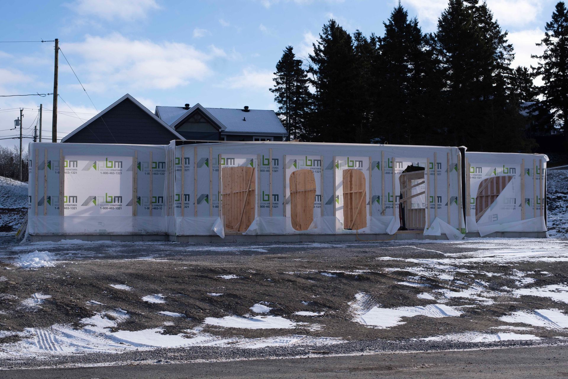 Maison partiellement charpentée en construction sur un terrain rural enneigé au crépuscule