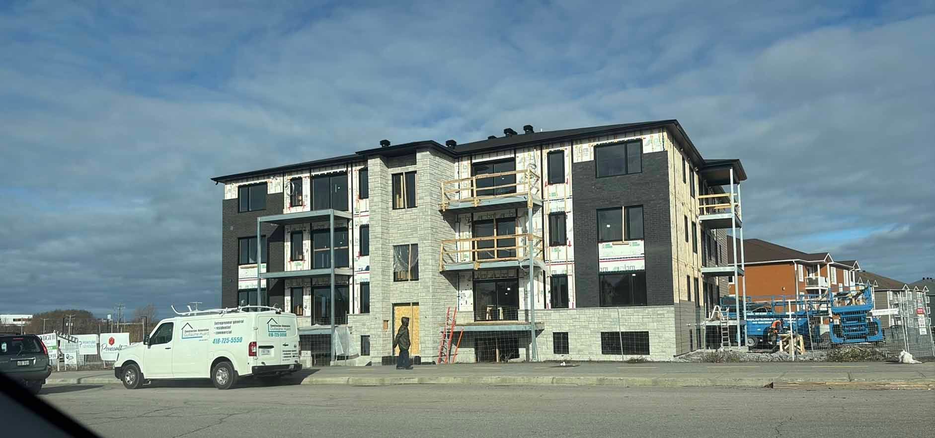 Immeuble d'appartements endommagé, fenêtres condamnées et véhicules stationnés sous un ciel nuageux