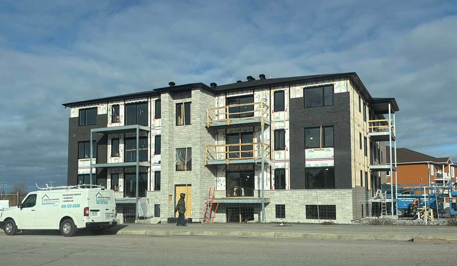 Immeuble d'appartements en construction avec des engins de chantier et des ouvriers en bord de route