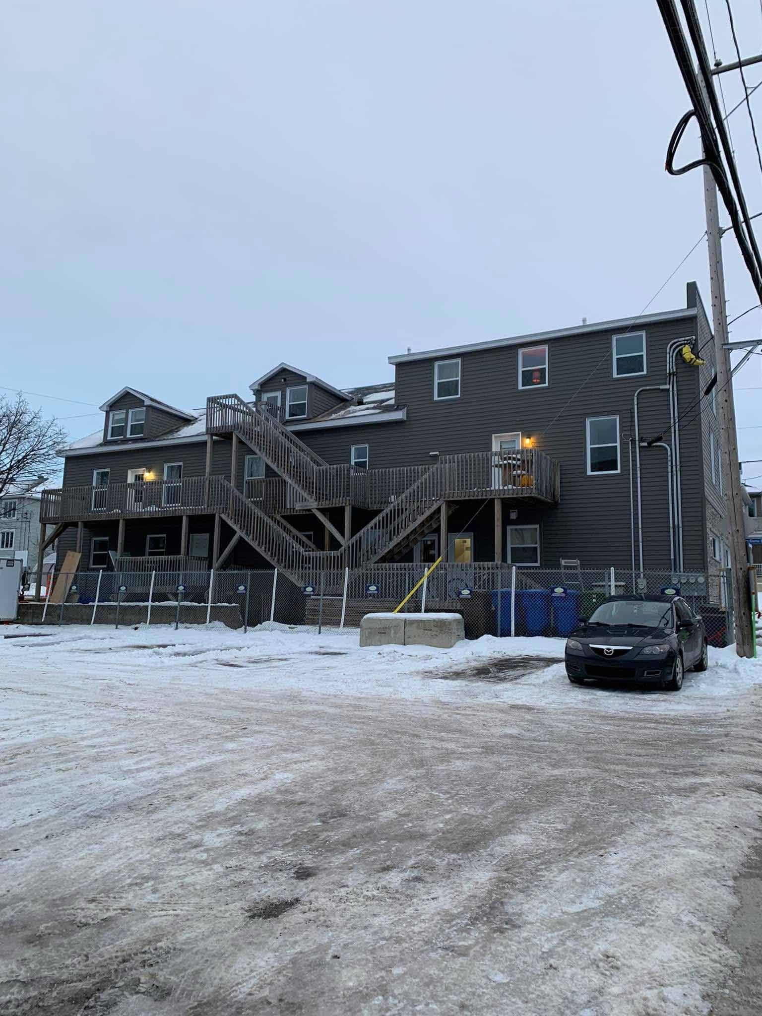Parking enneigé à côté d'un immeuble d'appartements marron avec escalier extérieur et voitures garées