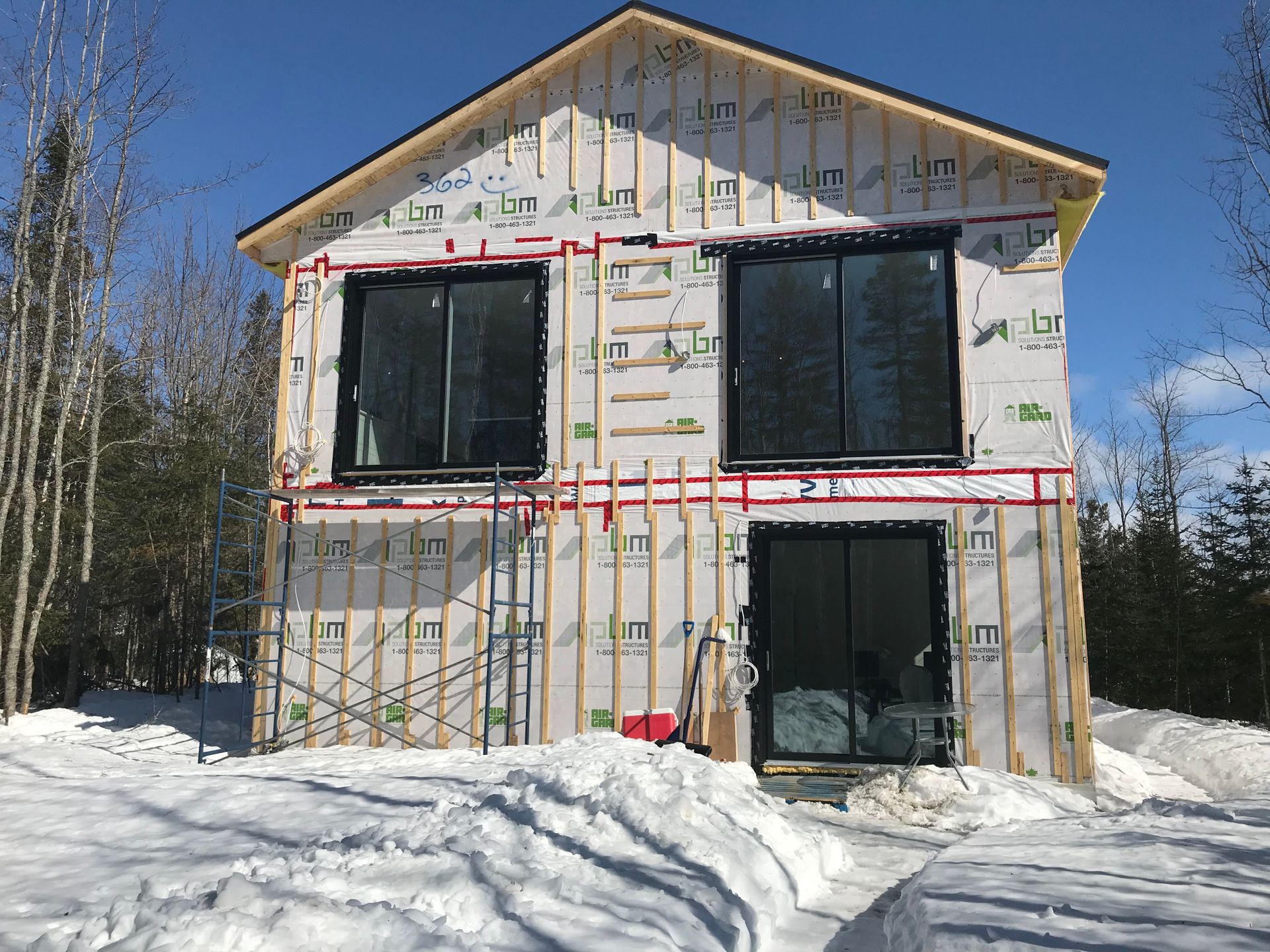 Une maison est en construction dans la neige avec beaucoup de fenêtres.