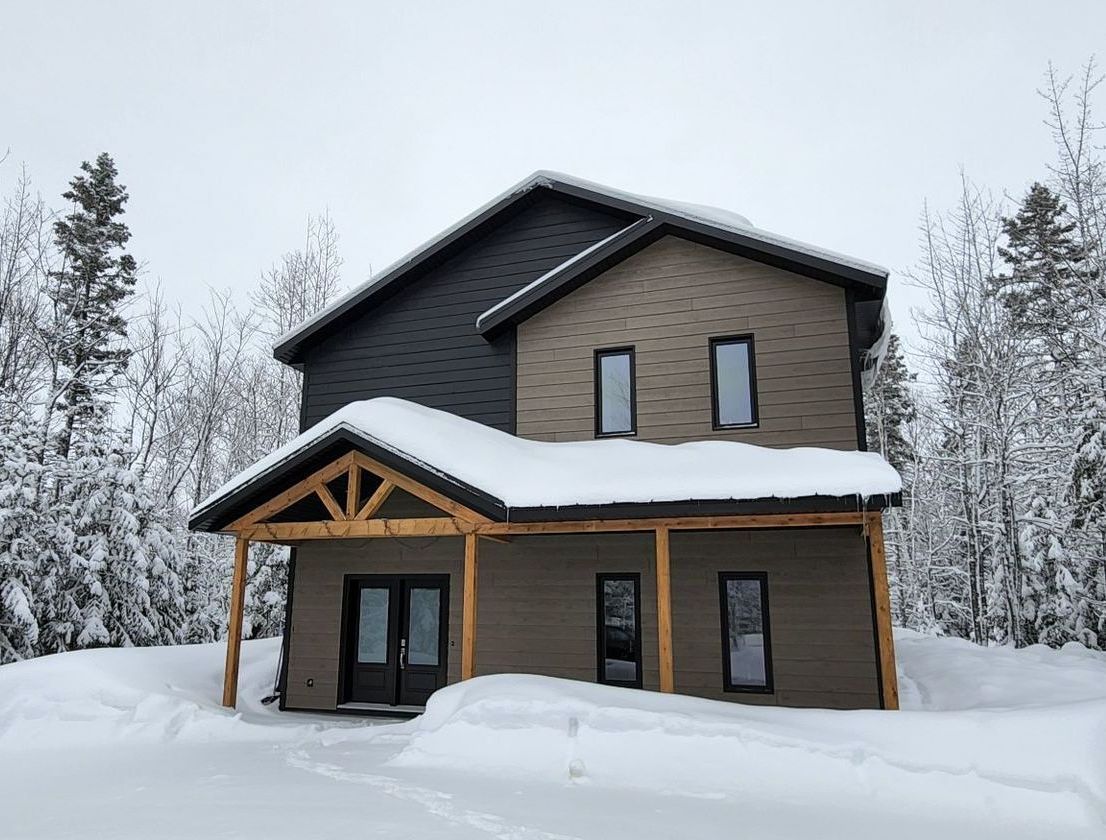 Une maison est recouverte de neige au milieu d'une forêt enneigée.