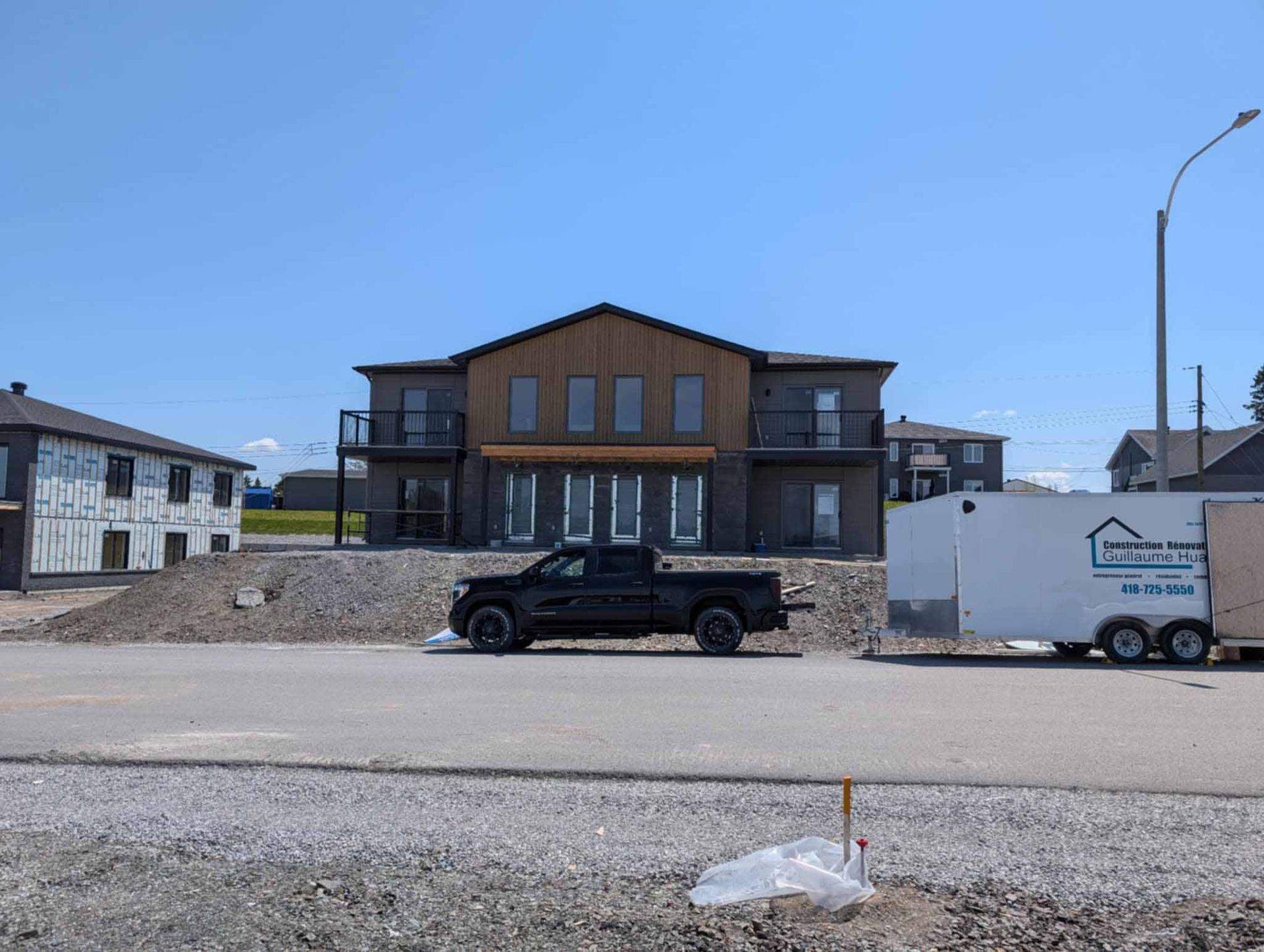Maison à deux étages en construction derrière un mur de soutènement en pierre, avec un SUV noir garé devant.