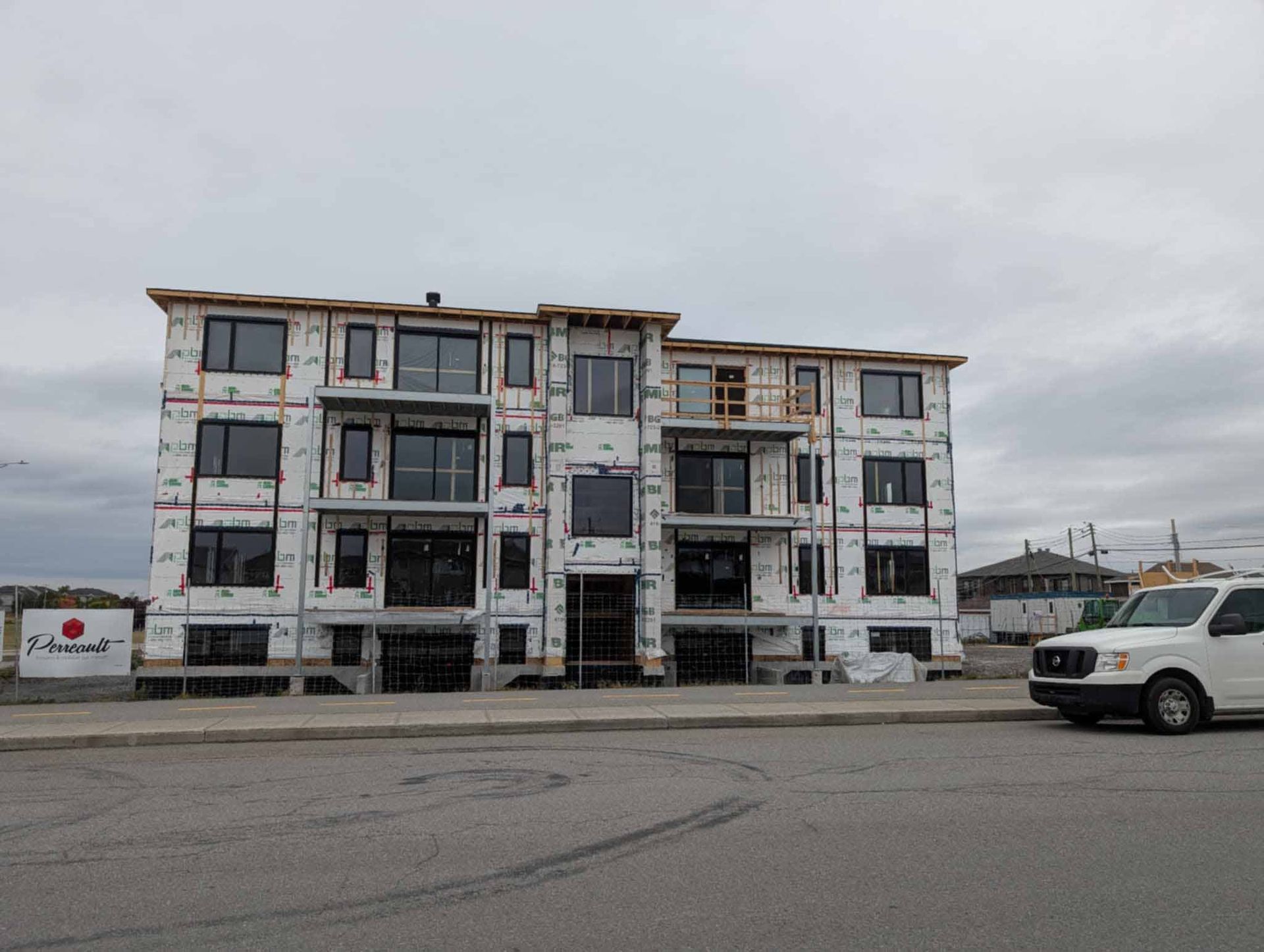Un immeuble d'appartements de quatre étages en construction par temps nuageux, avec une camionnette blanche garée à proximité.