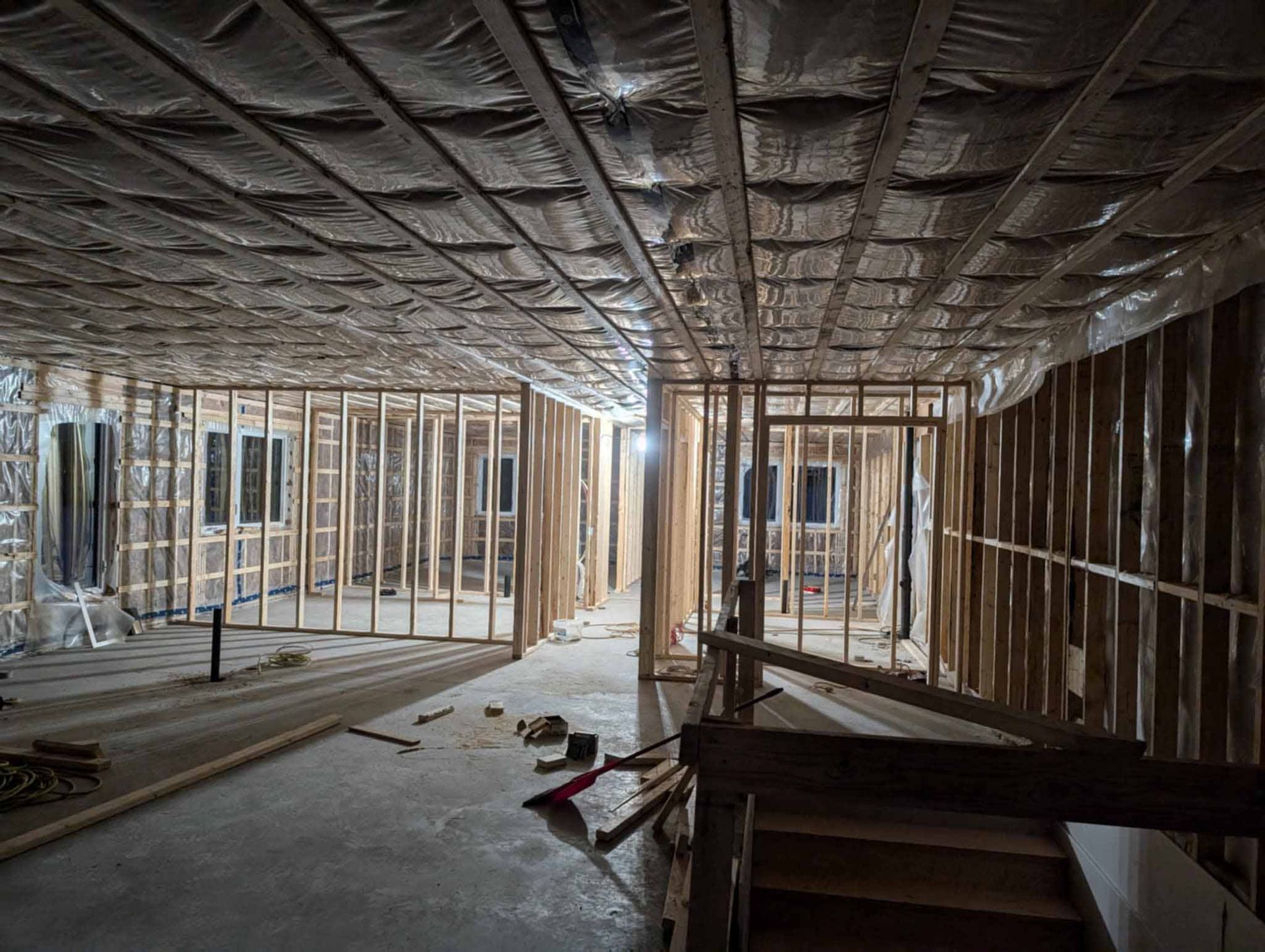 Intérieur d'un bâtiment en construction, partiellement ossature bois, avec murs apparents, isolation du plafond et outils éparpillés.
