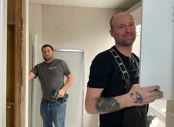 Deux hommes travaillent dans une salle de bain et l'un d'eux a un tatouage sur le bras