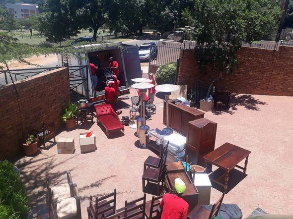 Backyard patio with scattered furniture, brick walls, and two people near a shaded gate area