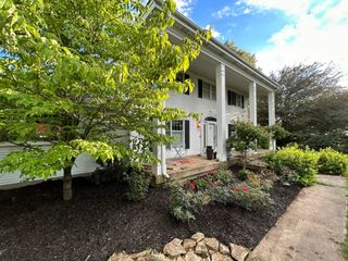 White house with large columns, front porch, and garden. Trees and blue sky.