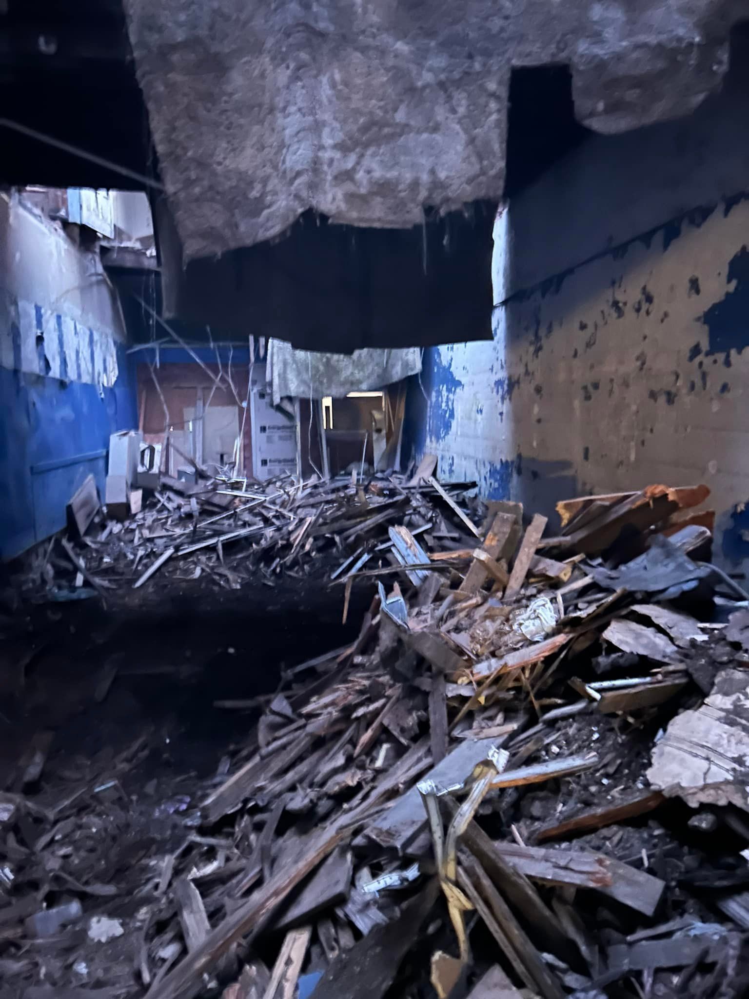 Pile of debris in a demolished building. Dark, blue walls and ceiling with sections missing.