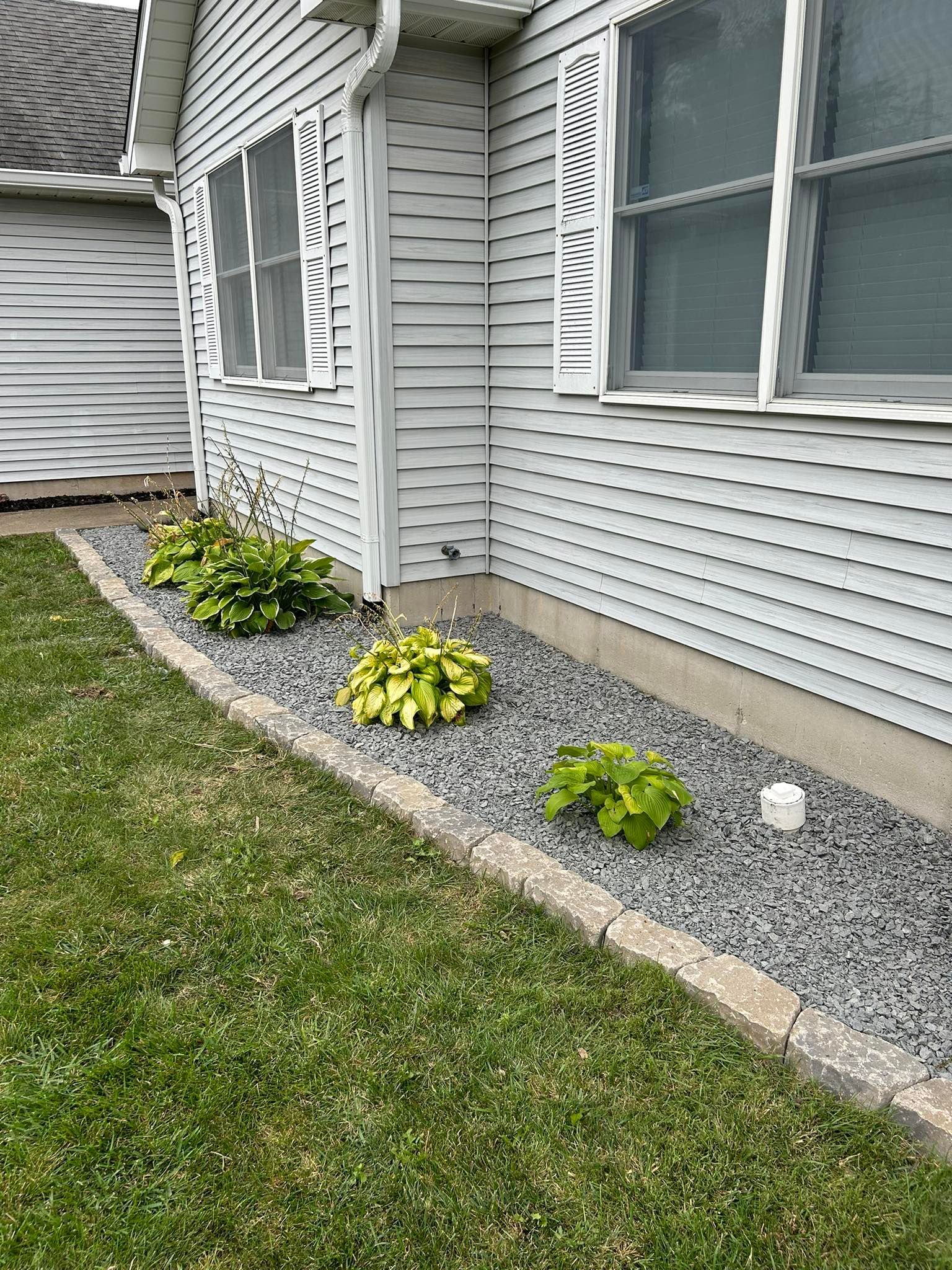 Exterior view of a house with a flower bed of green plants and gray gravel bordered by concrete.