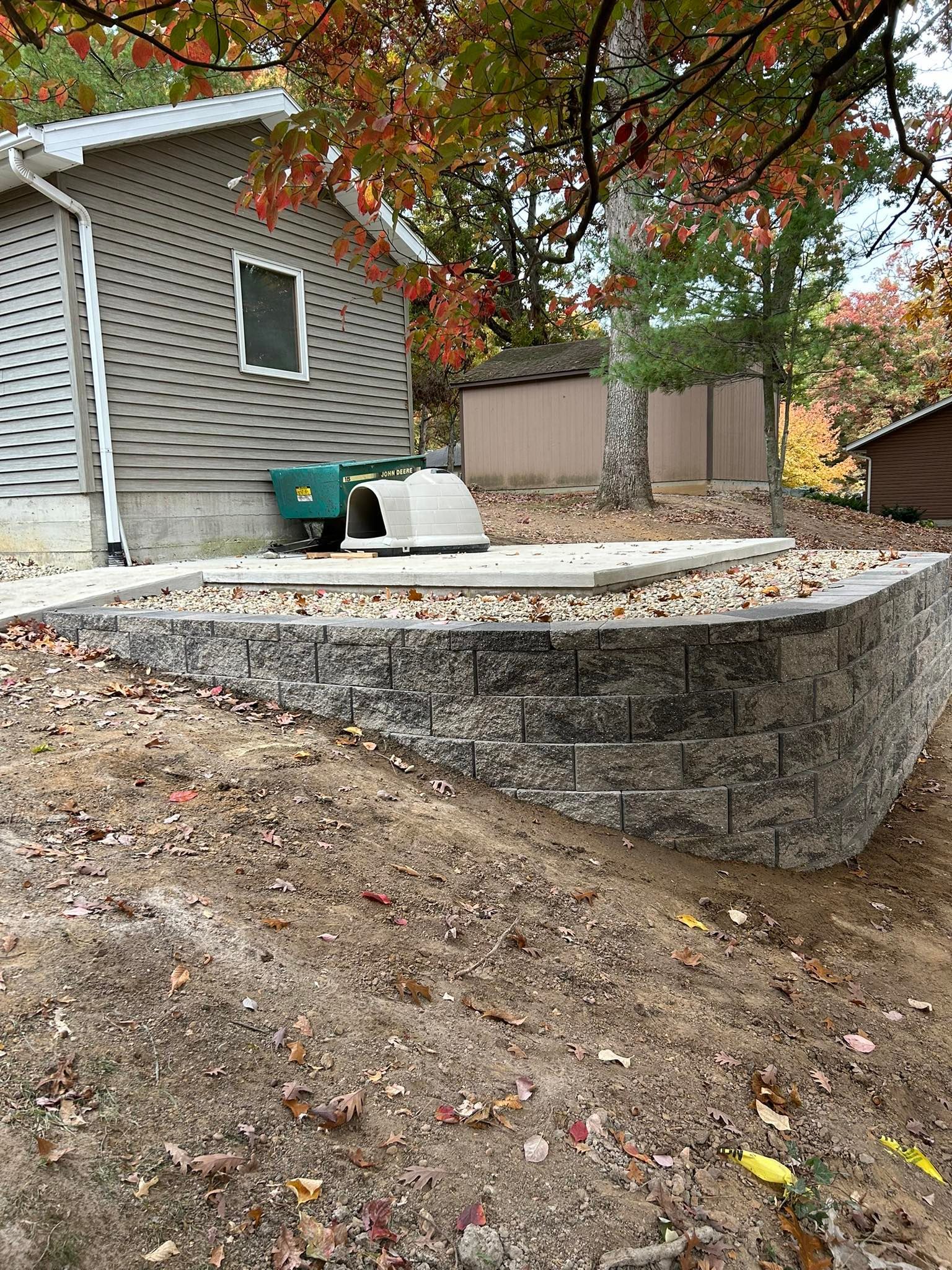 Stone retaining wall and concrete patio next to a house with fall foliage.
