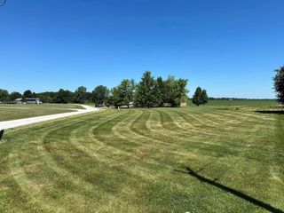 Lawn with curved mowing pattern, trees, a walking path, and a clear blue sky.