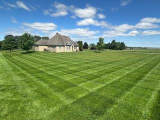 Lawn mowed in a chevron pattern in front of a tan brick house under a blue sky with clouds.