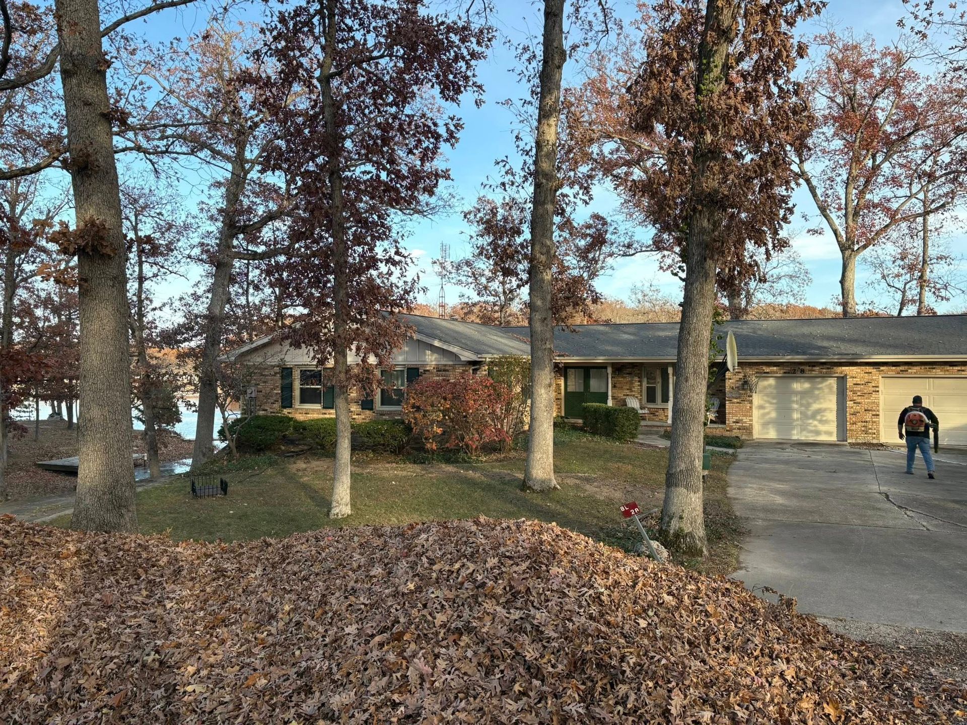 House with fall foliage, trees, driveway, and person standing.