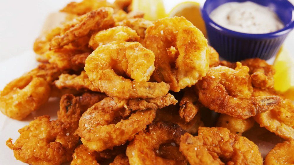 A plate of fried shrimp with a dipping sauce and lemon wedges.