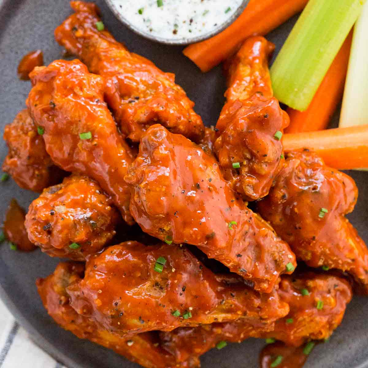 A close up of a plate of buffalo chicken wings with carrots and celery.