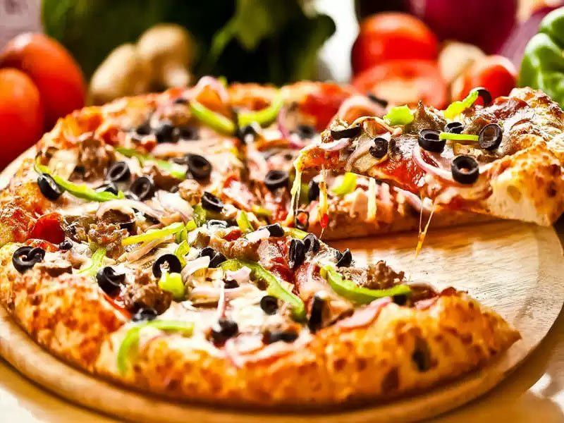A pizza with a slice taken out of it is on a wooden cutting board.