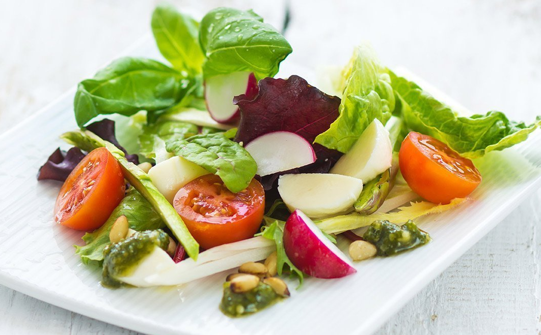 A white plate topped with a salad of lettuce tomatoes and radishes.