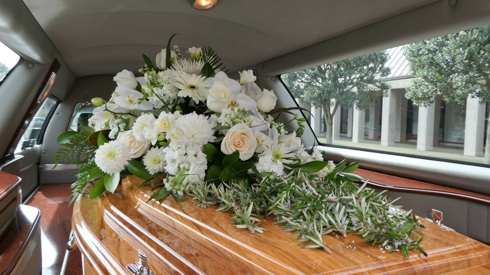 A Coffin Is Sitting in The Back of A Limousine with White Flowers — Pick-A-Bunch Florists & Gifts In Sarina, QLD