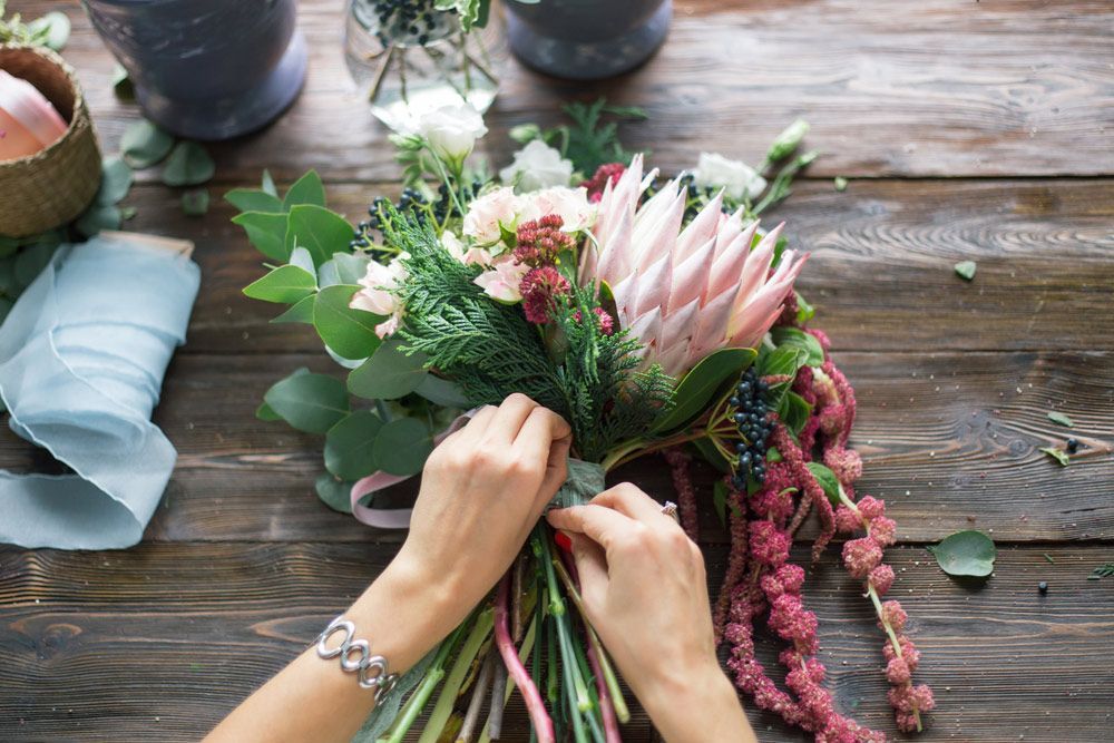 A Woman Is Making a Bouquet of Flowers on A Wooden Table — Pick-A-Bunch Florists & Gifts In Armstrong Beach, QLD