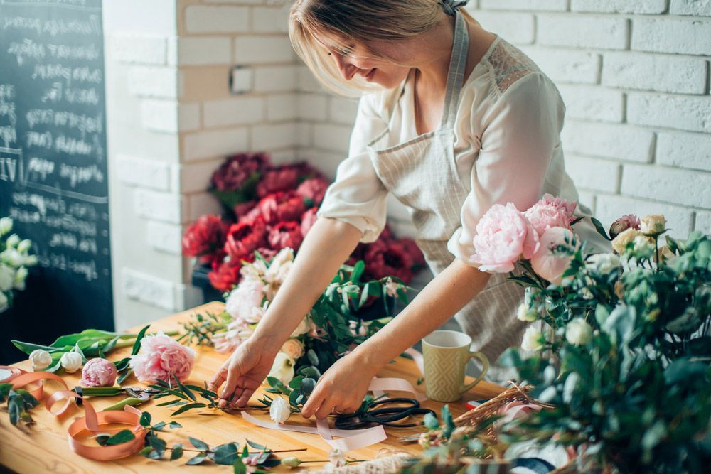 A Woman Is Making a Bouquet of Flowers on A Table — Pick-A-Bunch Florists & Gifts In Sarina, QLD