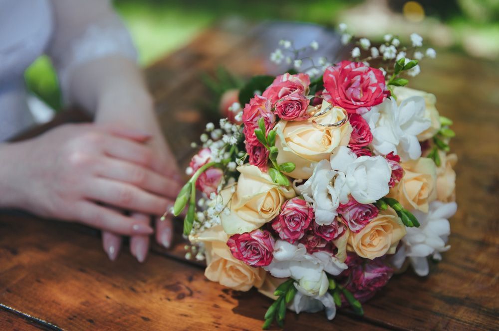 A Woman Is Holding a Bouquet of Flowers on A Wooden Table — Pick-A-Bunch Florists & Gifts In Koumala, QLD